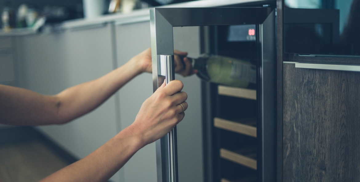 A woman's arm reaches into a wine fridge to remove a bottle of white wine, picture