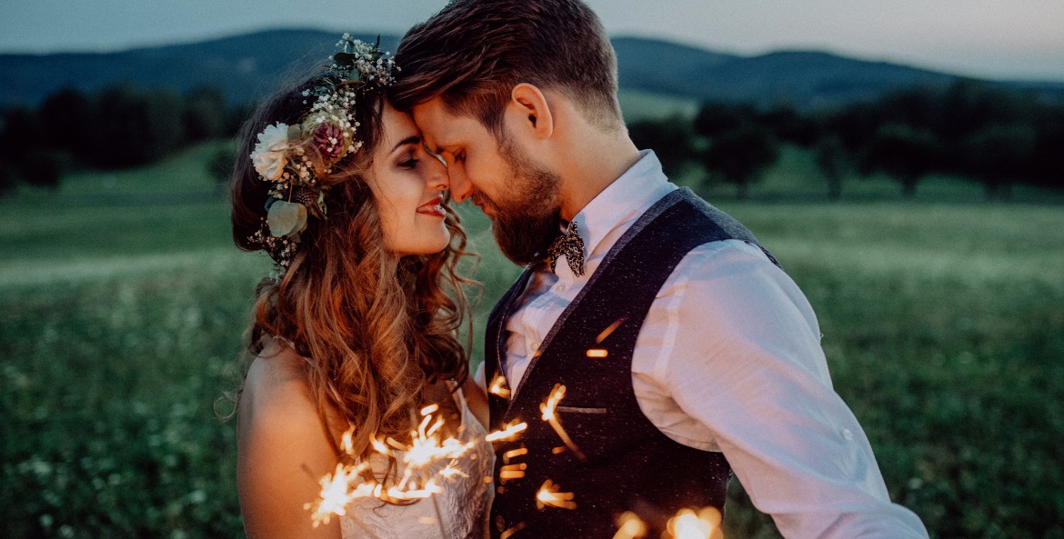 Man and woman kiss after wedding reception with sparklers.