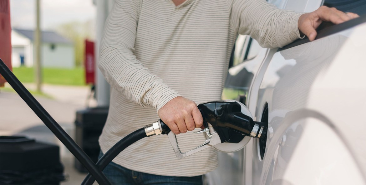 man filling white car with fuel.
