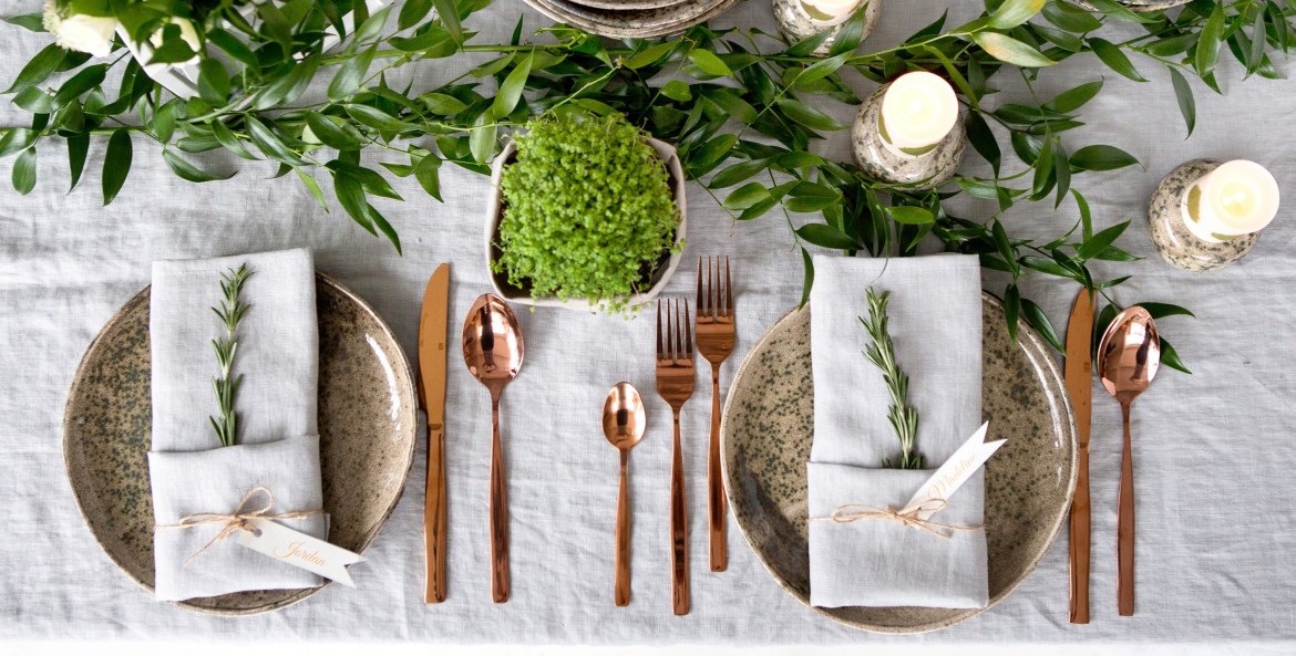 Greenery, candles, and flowers on a holiday table with rose gold silverware
