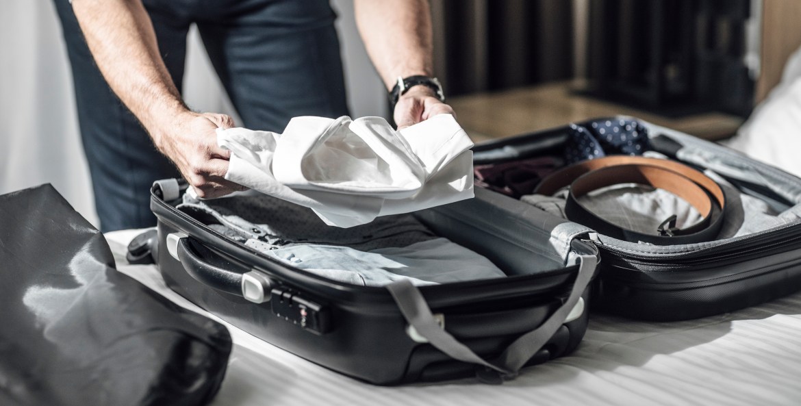 A business man packs a rolling carry-on suitcase on a white bedspread, image