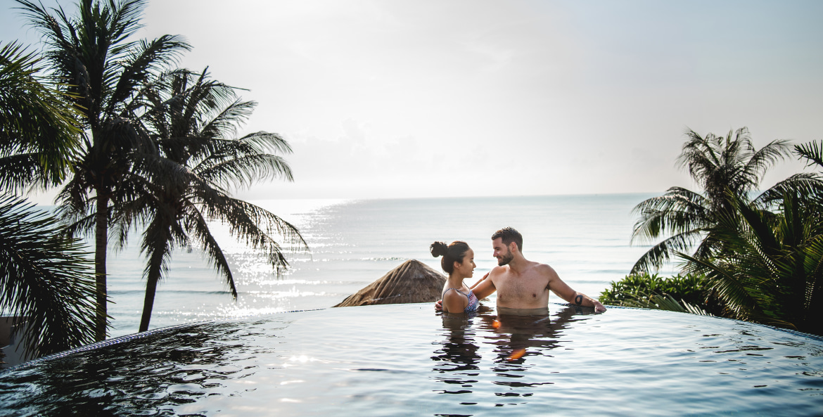 picture of a happy couple in an infinity pool near palm trees at sunset