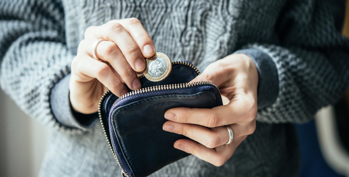 A close-up of a woman in a gray knit sweater puts euros into a purse.