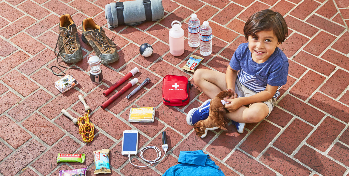 boy seated on ground with an array of emergency road kit essentials, picture