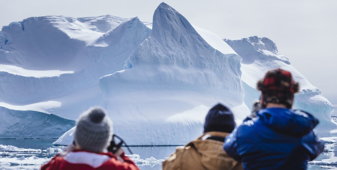 three people wearing coats and caps view glacier from boat, picture