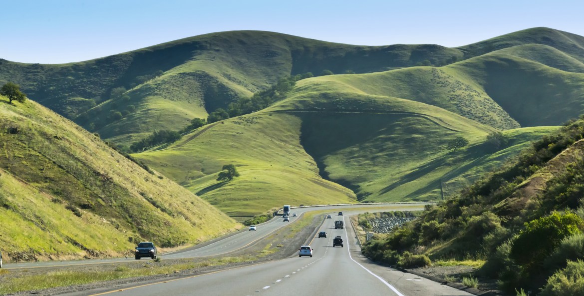 autos on divided highway with green hills in background, picture