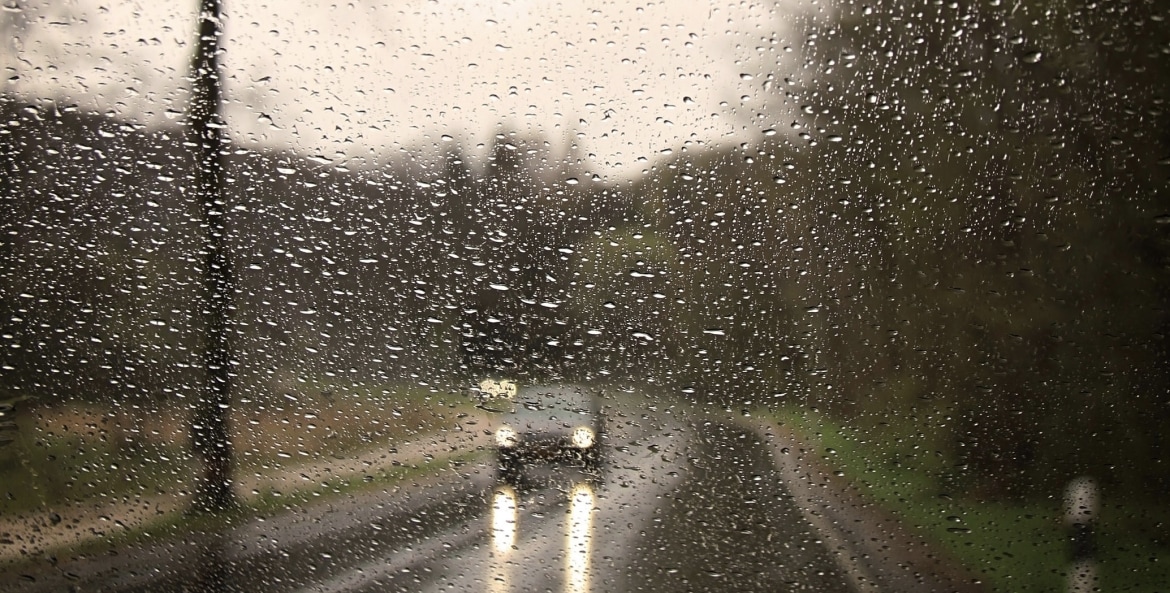 car driving on a wet road seen through a rainy windshield
