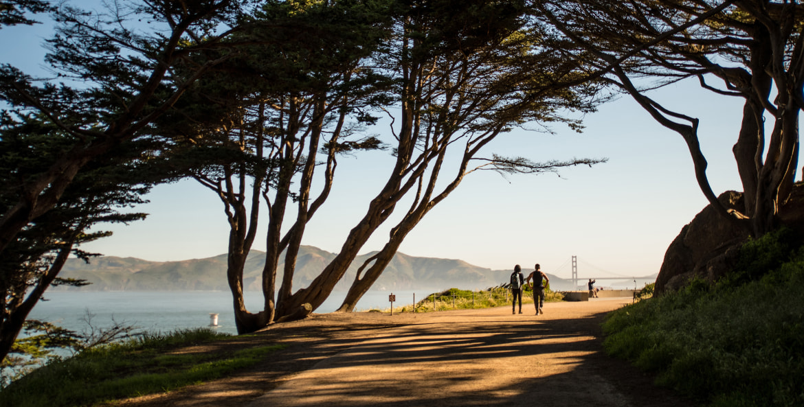 picture of a couple walking a path in the presidio with the golden gate bridge in the background