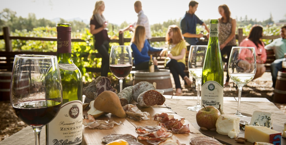Picnic spread of wine, cheese, and meats set amid visitors at a California winery, photo
