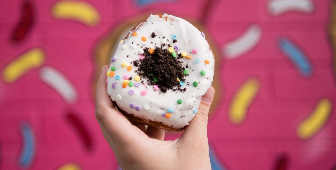 A hand holds a Oh My Birthday Cake Oreo stuffed donut from the Las Vegas Donut Bar, image