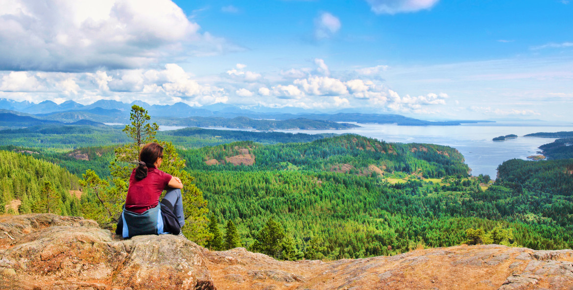 A woman sits on a mountain overlooking Vancouver Island in British Columbia, image