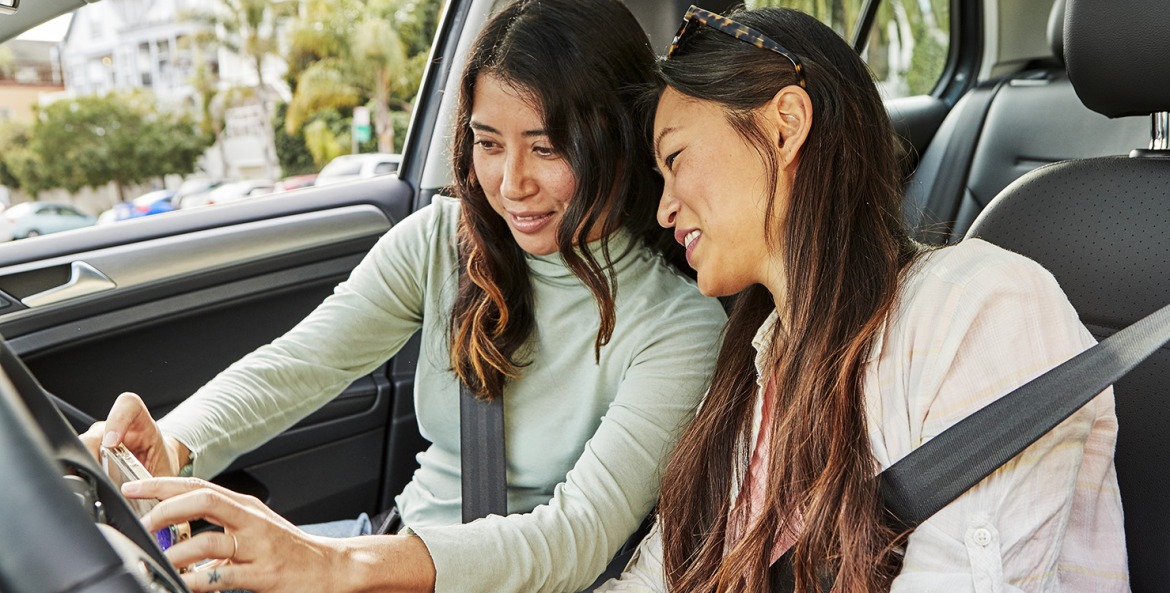 two women in parked car looking at mobile device, picture