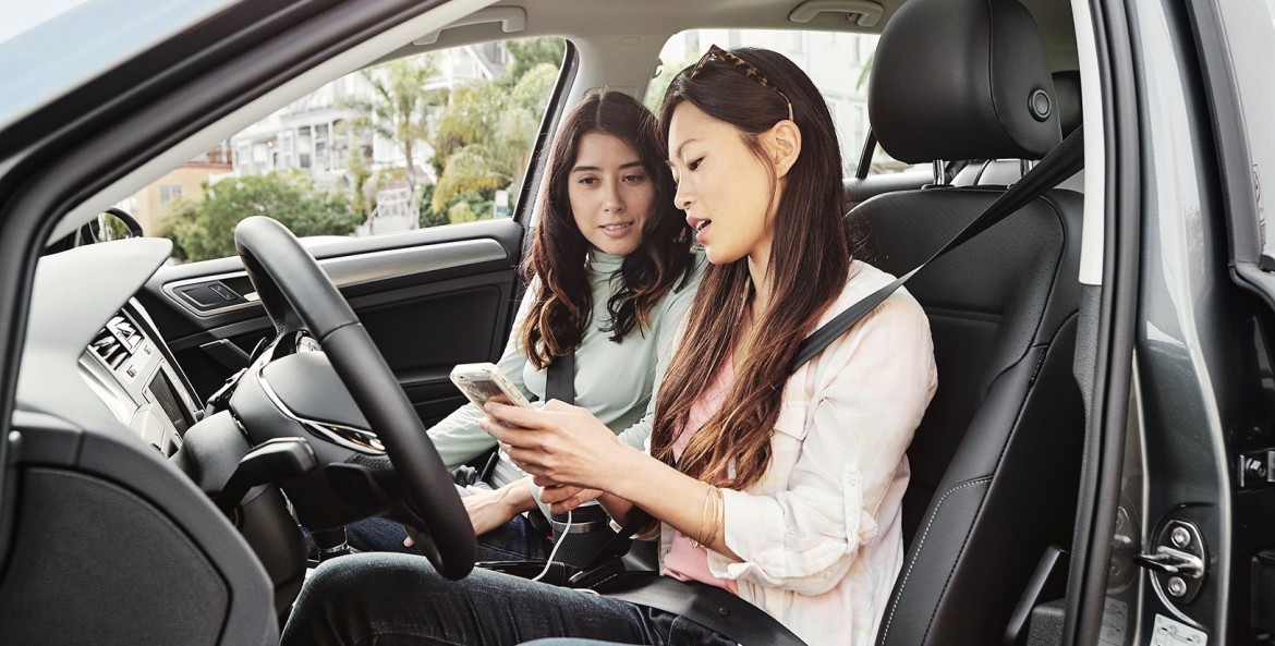 two young women look at a cell phone in a car