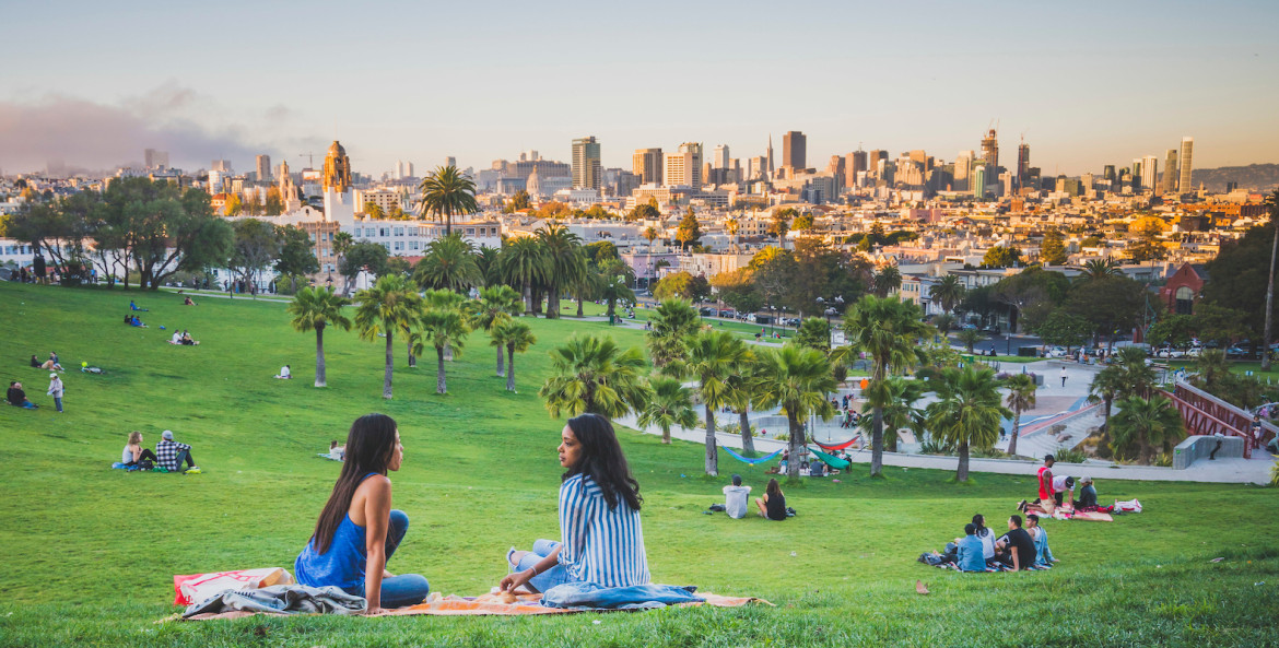 people sit on the grass at dolores park, with view of san francisco, picture