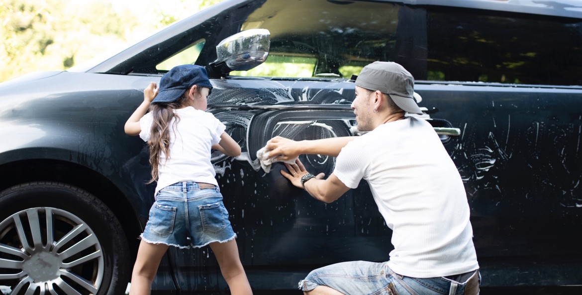 father and daughter in jeans, t-shirts-and baseball hats wash the exterior of the family car