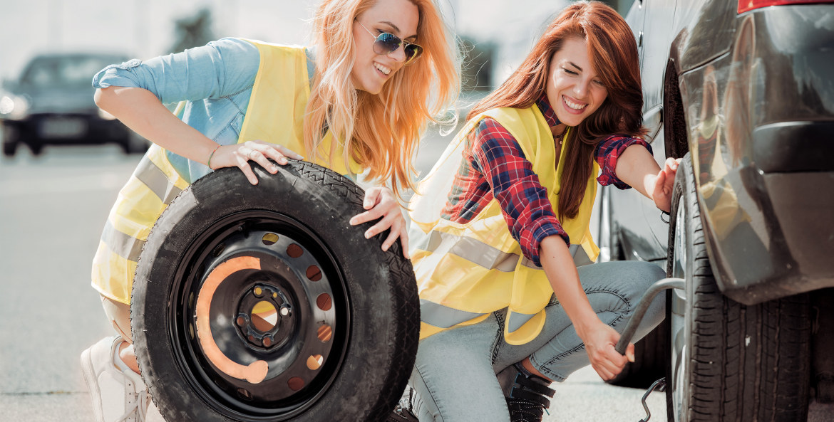 two young women wearing safety vests change a flat tire