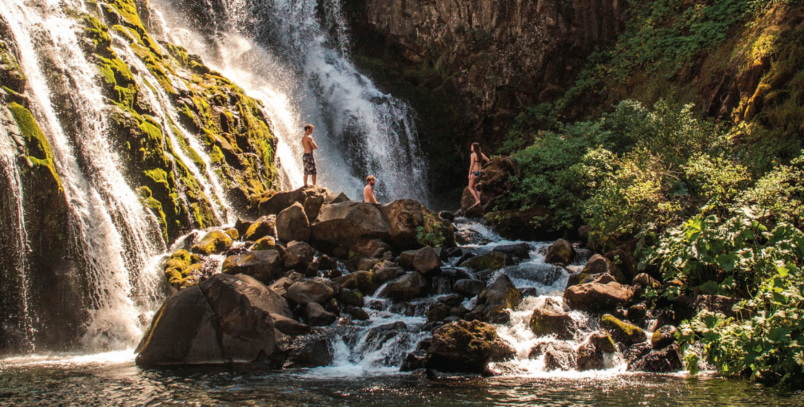 trio of swimmers admire Middle Falls from rocks below on the McCloud River near Mt Shasta, California, picture