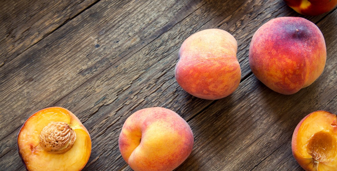 fresh organic peaches, whole and halved with pits, loosely arranged on rustic wooden background