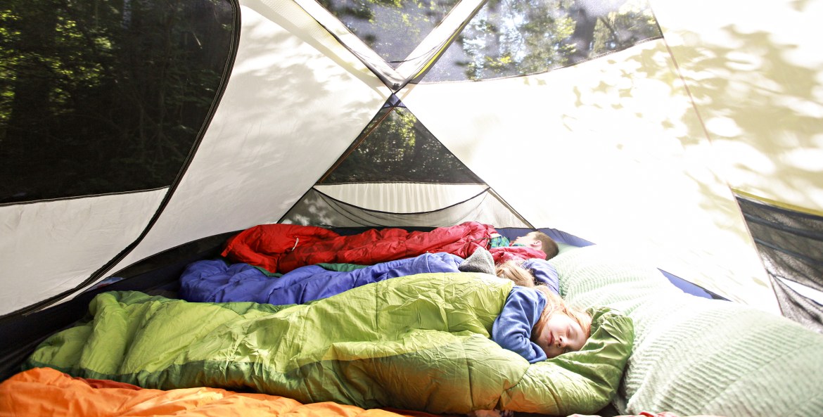Children sleep in sleeping bags inside a bright tent