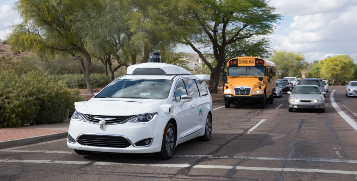 A Waymo driverless vehicle stops at an intersection with a school bus.