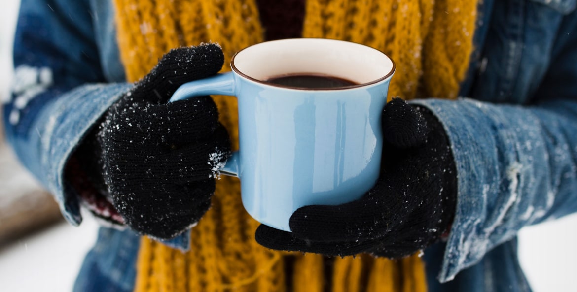 A person holds a blue coffee mug on a snowy morning.