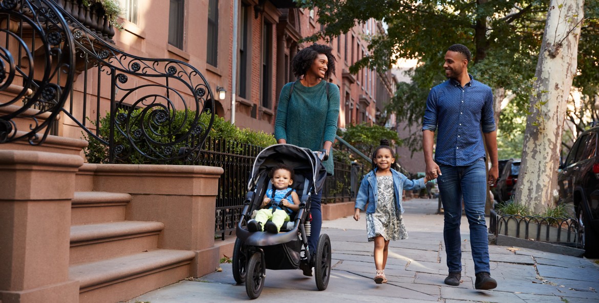 Family walks down a street in New York with a young girl and a baby in a stroller.