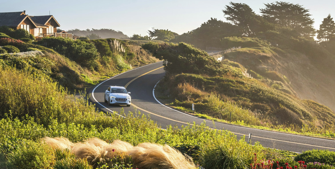An Audi E-Tron sedan navigates a curve along the coast on a sunny afternoon near Mendocino, California