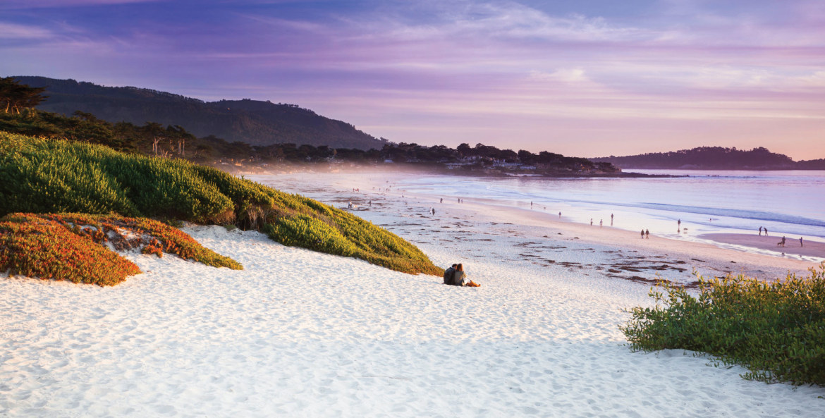 A couple sits on a beach at sunset in Carmel-by-the-Sea, California