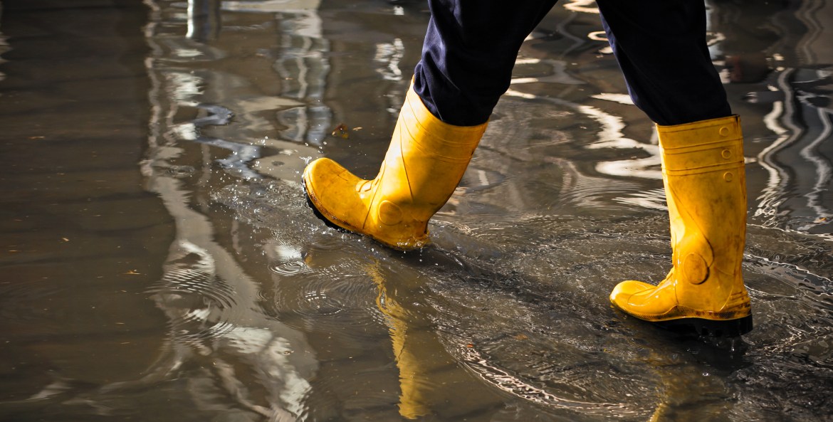 Close up view of a person in yellow rain boots walking through a flooded home
