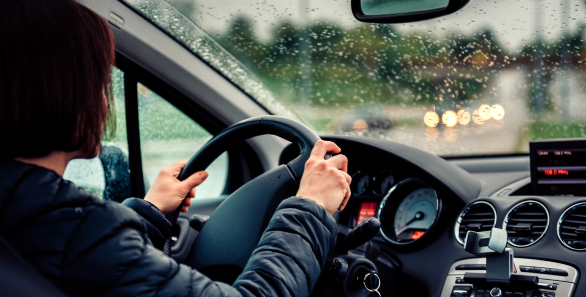 A woman grips the steering wheel with two hands while driving in the rain.