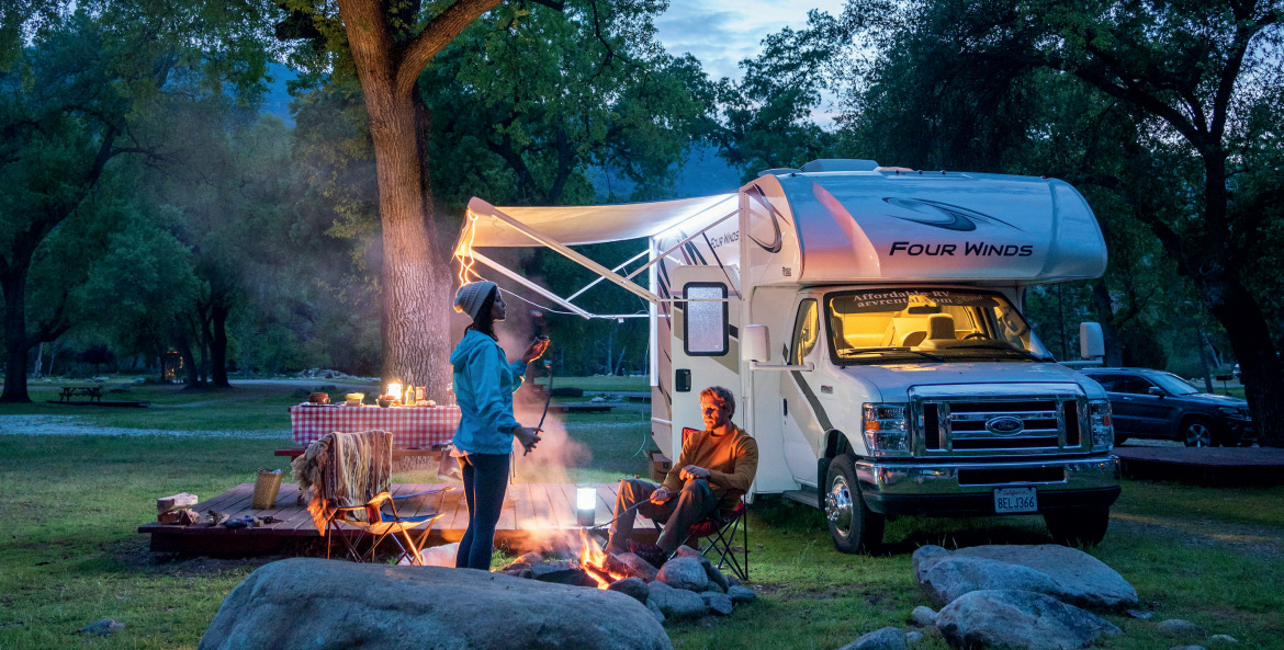 A couple relax around a campfire outside their RV