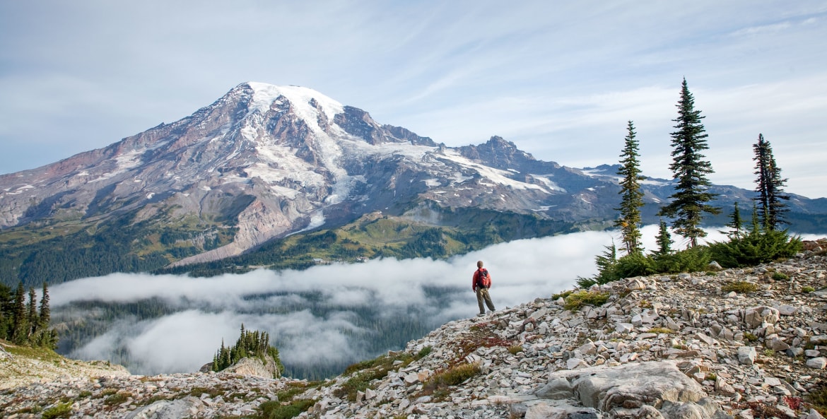 solo hiker takes in the panoramic view of Mount Rainier from Pinnacle Peak Trail in Washington