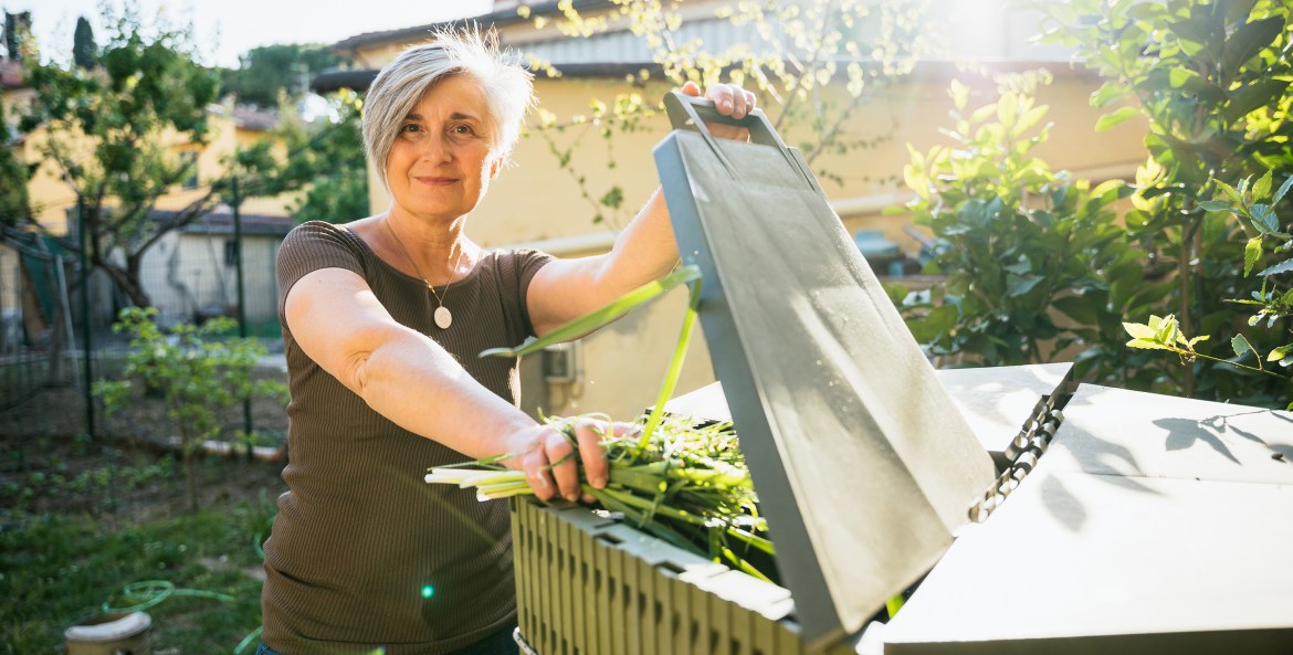 A woman puts greens into her backyard compost bin.