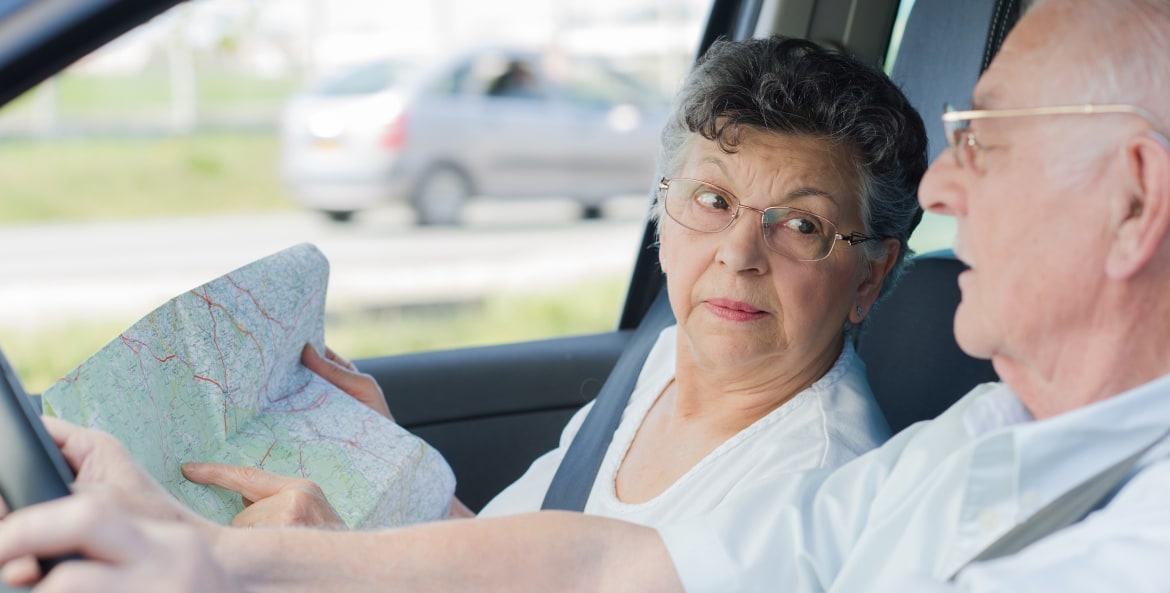 Elderly couple in car with wife pointing to map