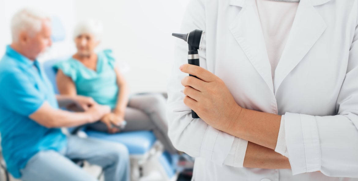 Doctor holds up otoscope while senior patients sit in background