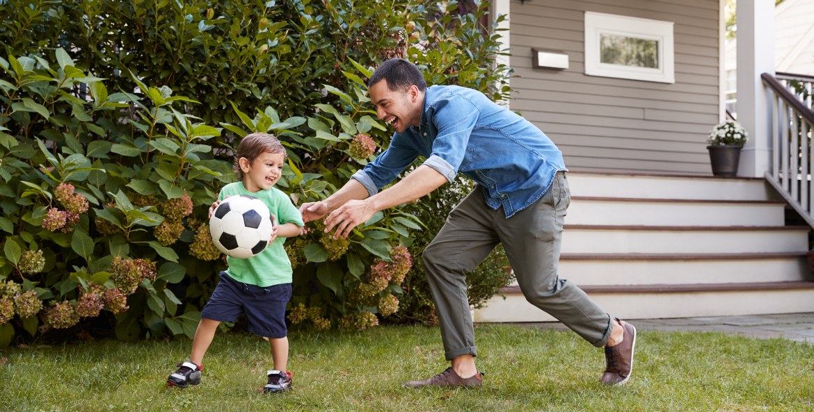 A father plays with his son in the front yard.