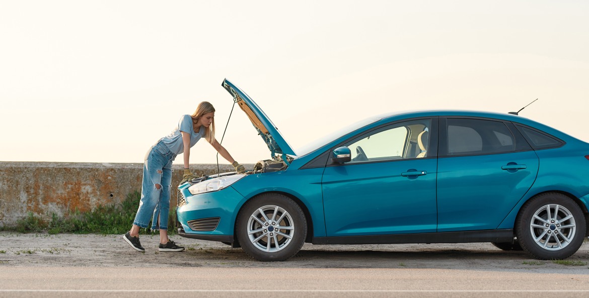 A woman looks under the hood of her overheated car.