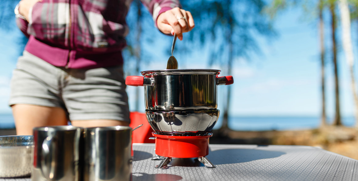A woman cooks on her camping stove on a picnic table.