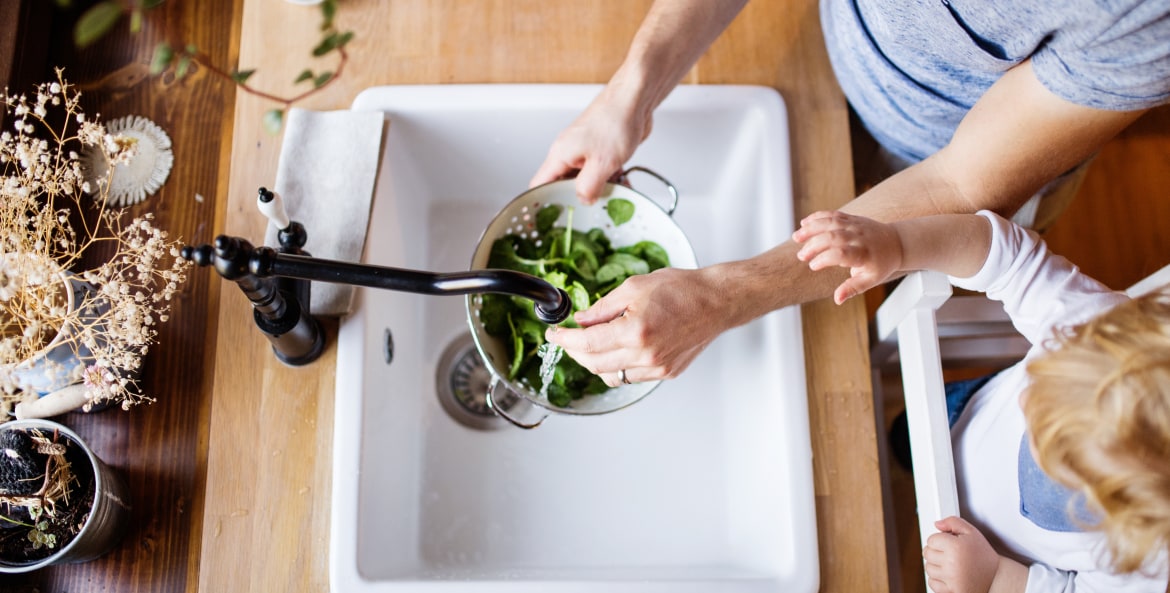 A father and his toddler wash spinach in their kitchen sink.