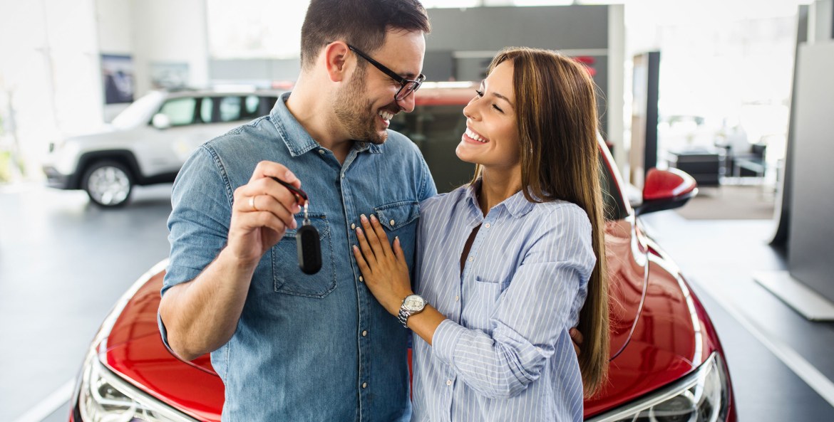 A couple hold the keys to their new red car in the dealership.