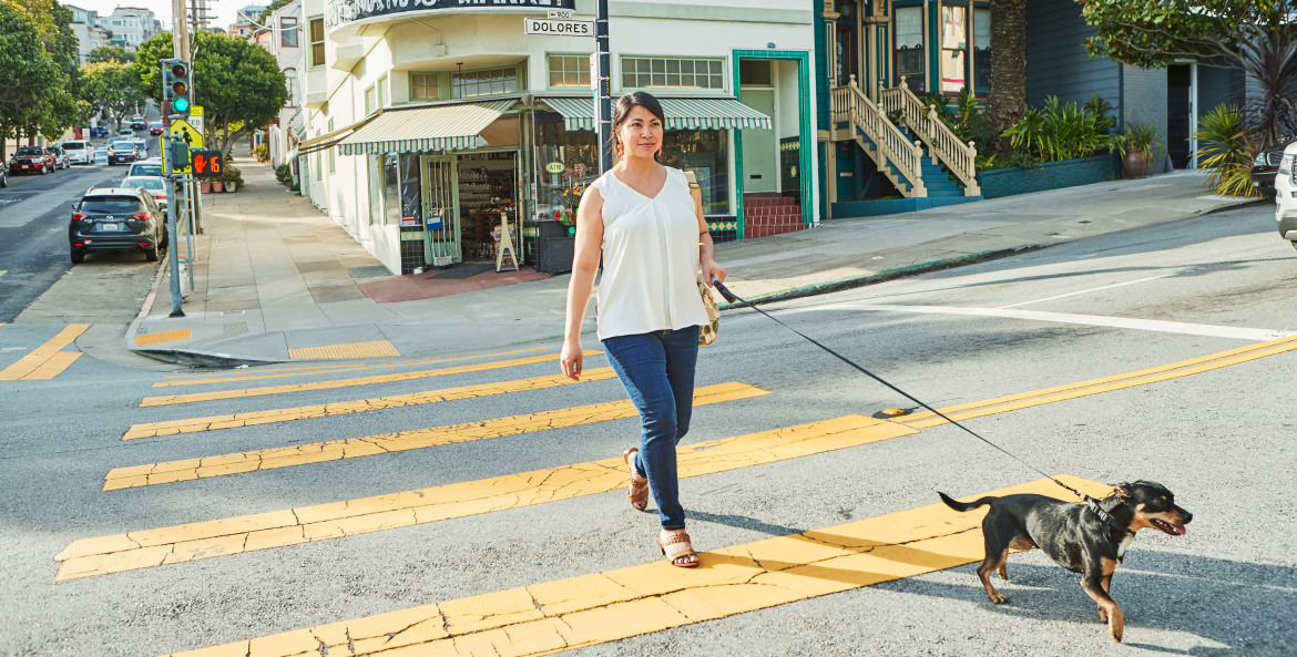 A woman crosses in the street with her small dog in San Francisco.