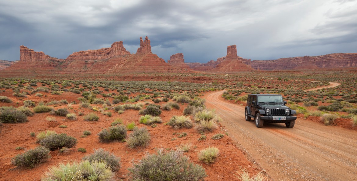 A Jeep drives on a dirt road through Valley of the Gods in Utah.