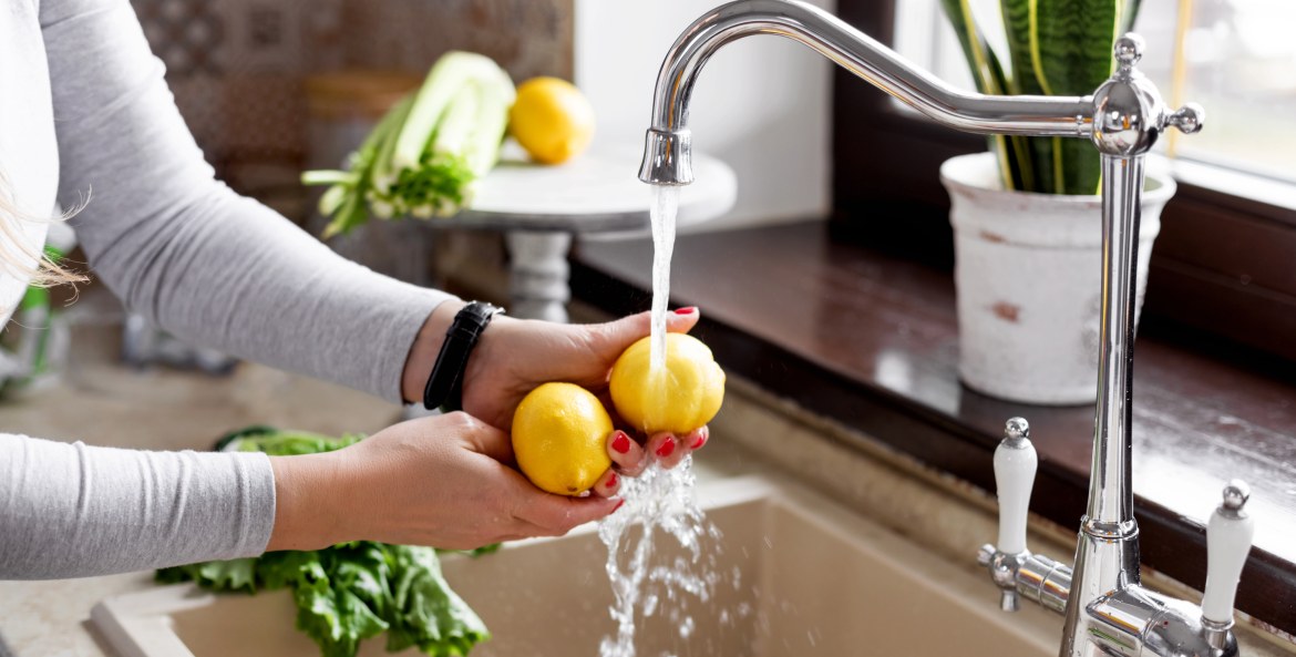 A woman washes lemon at the kitchen sink.