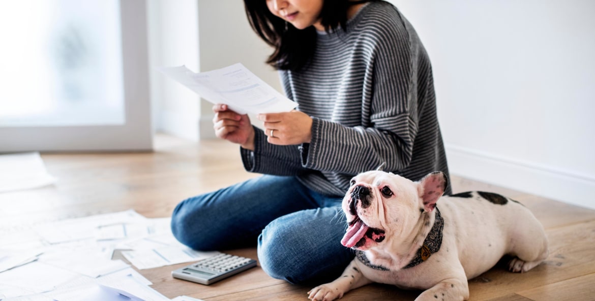 A woman sorts through her finances and calculates debt while sitting on the floor next to her small bulldog.