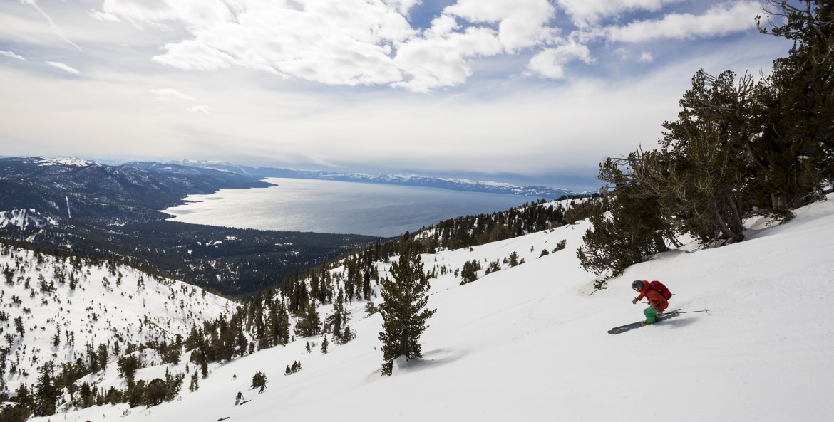 A skier rides down the mountain with views of Lake Tahoe in the background, image