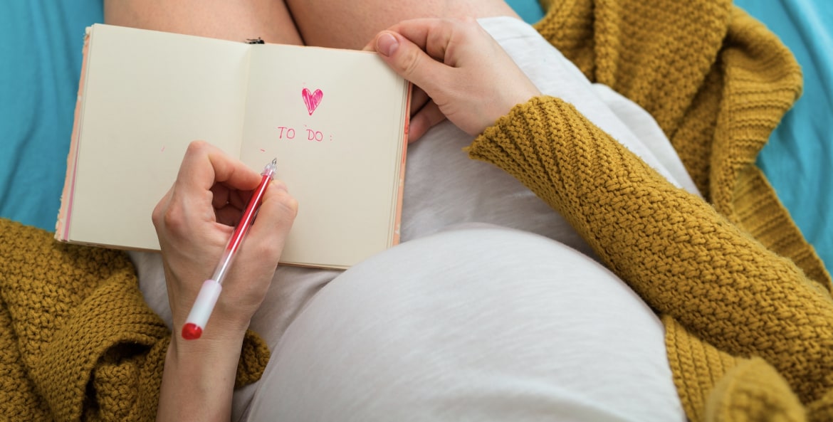 a pregnant woman writes a to-do list with a heart