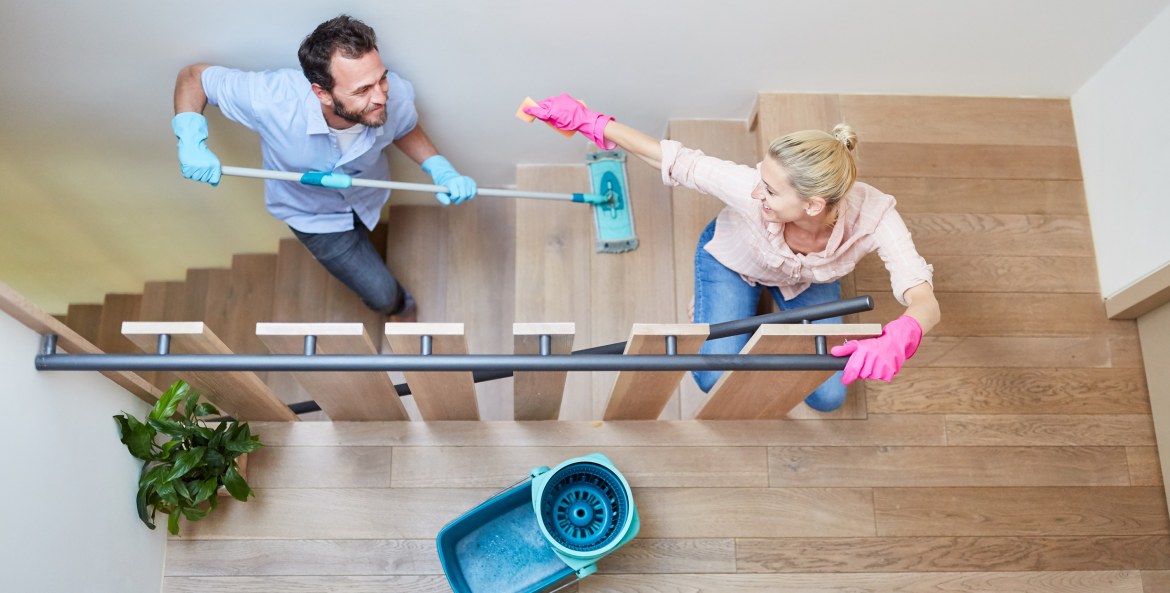white couple playfully run upstairs while mopping their wooden floors