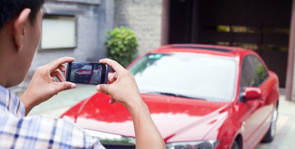 A man takes a picture of his red sedan to sell it.