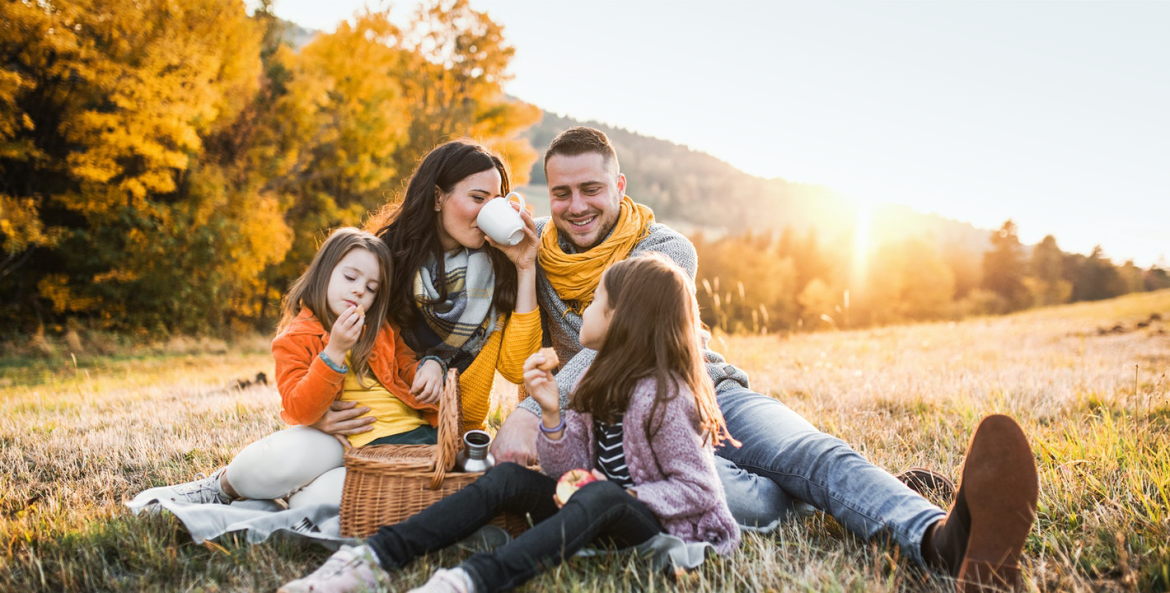 A family picnics in a field surrounded by yellow leaves.