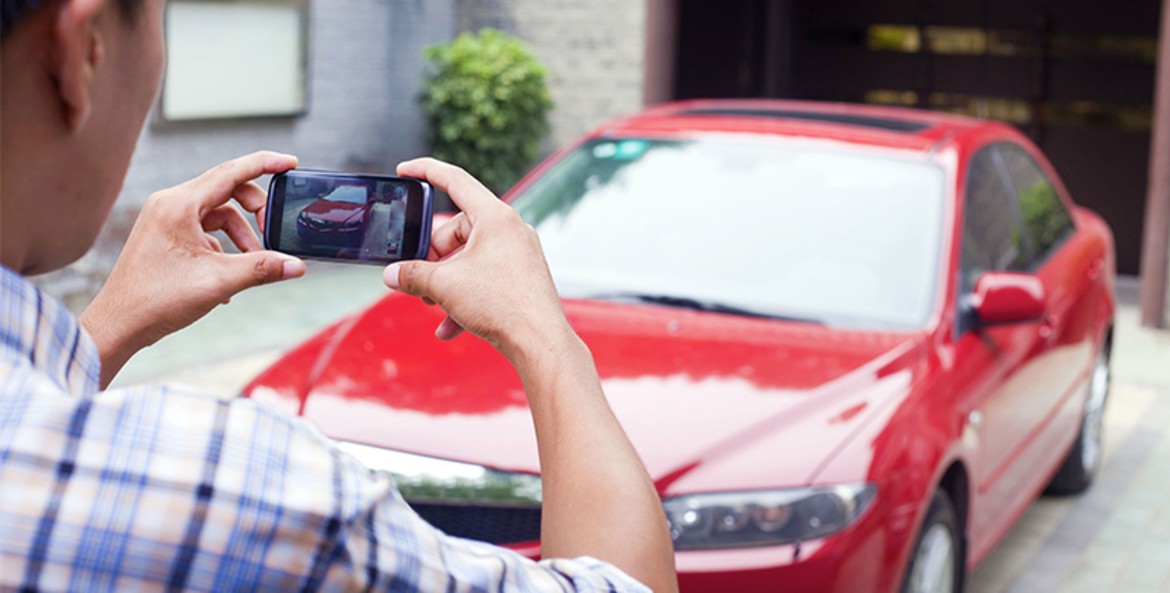 A man takes a picture of his red sedan to sell it.